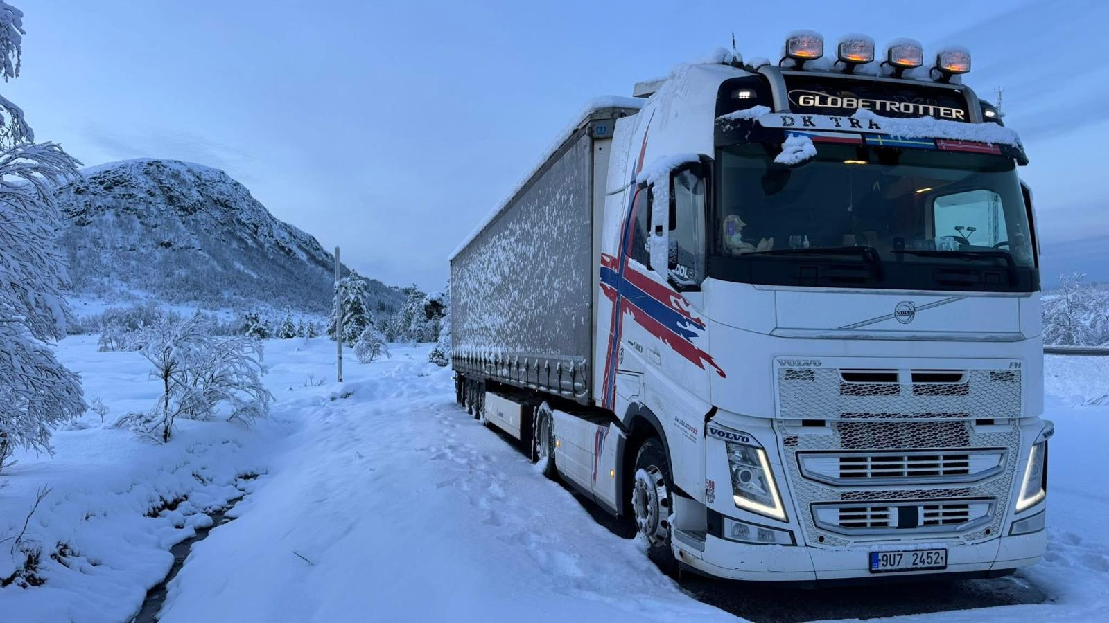 Bílý tahač DK Transport na zasněžené skandinávské trase